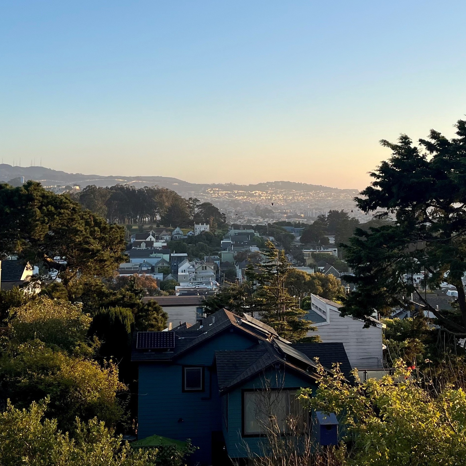 A view of San Francisco from Bernal Heights neighborhood there are trees to the right and residential properties to the left.